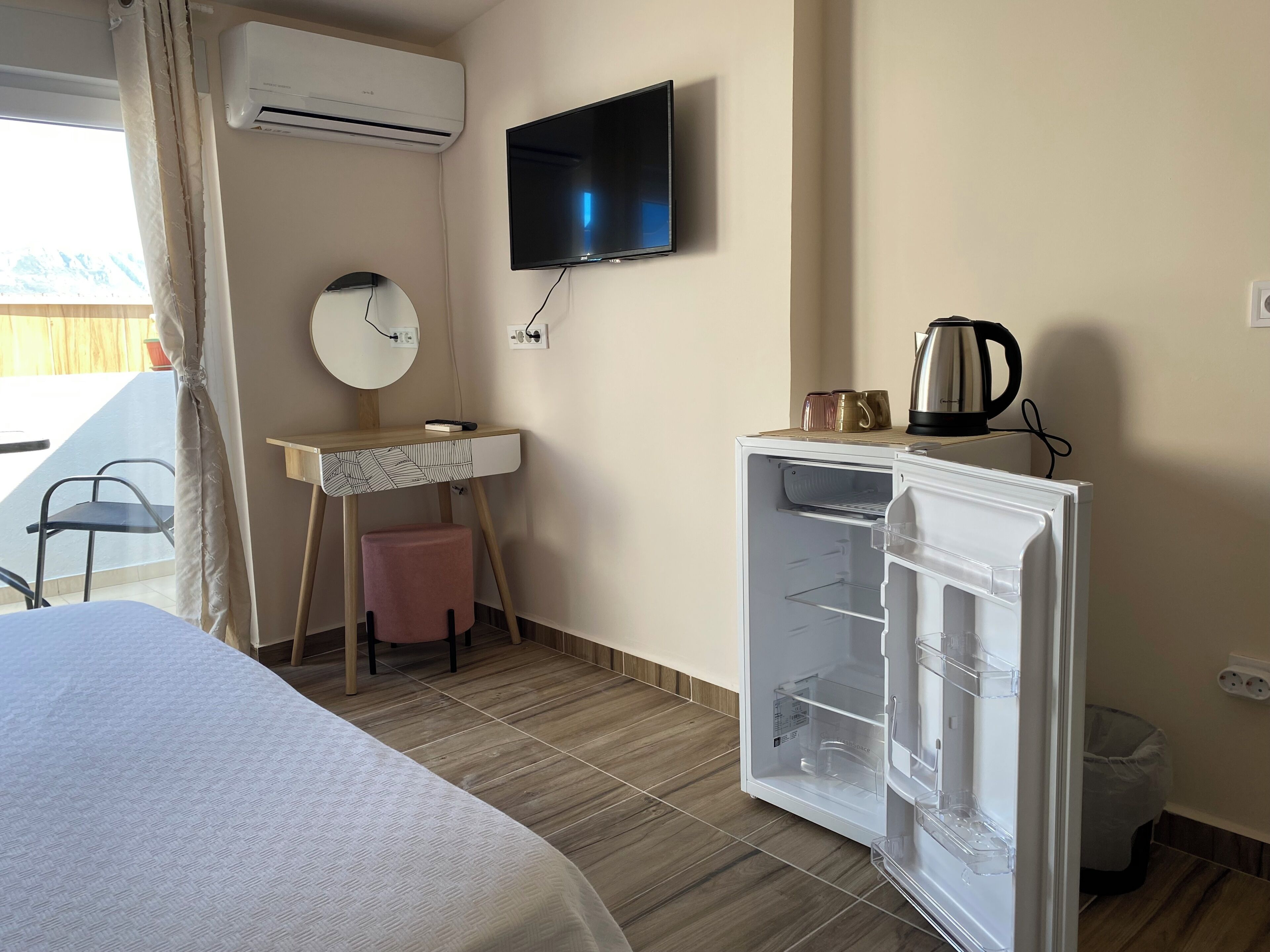 A hotel room with a bed, a desk with a chair, a television, a refrigerator, and a window with curtains.