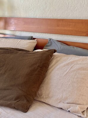 Un lit avec une tête de lit en bois et plusieurs oreillers de différentes couleurs.