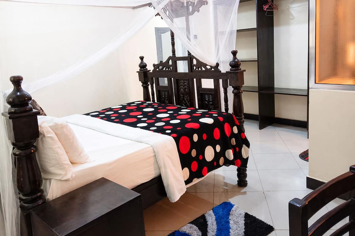 Una cama con dosel, una mesita de noche, una colcha estampada y una alfombra azul y blanca.