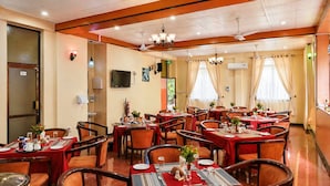 Un comedor de hotel con varias mesas, sillas y un televisor en la pared.
