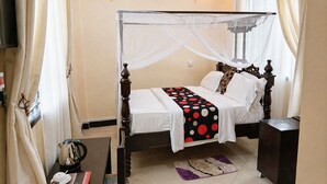Una cama con dosel, una mesita de noche, un aparador y una ventana con cortinas.