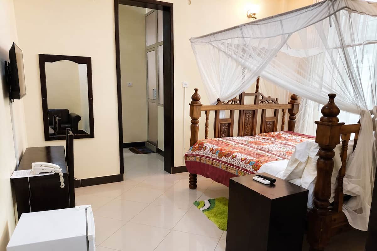 Una habitación de hotel con cama, mesita de noche, teléfono, espejo y televisor.