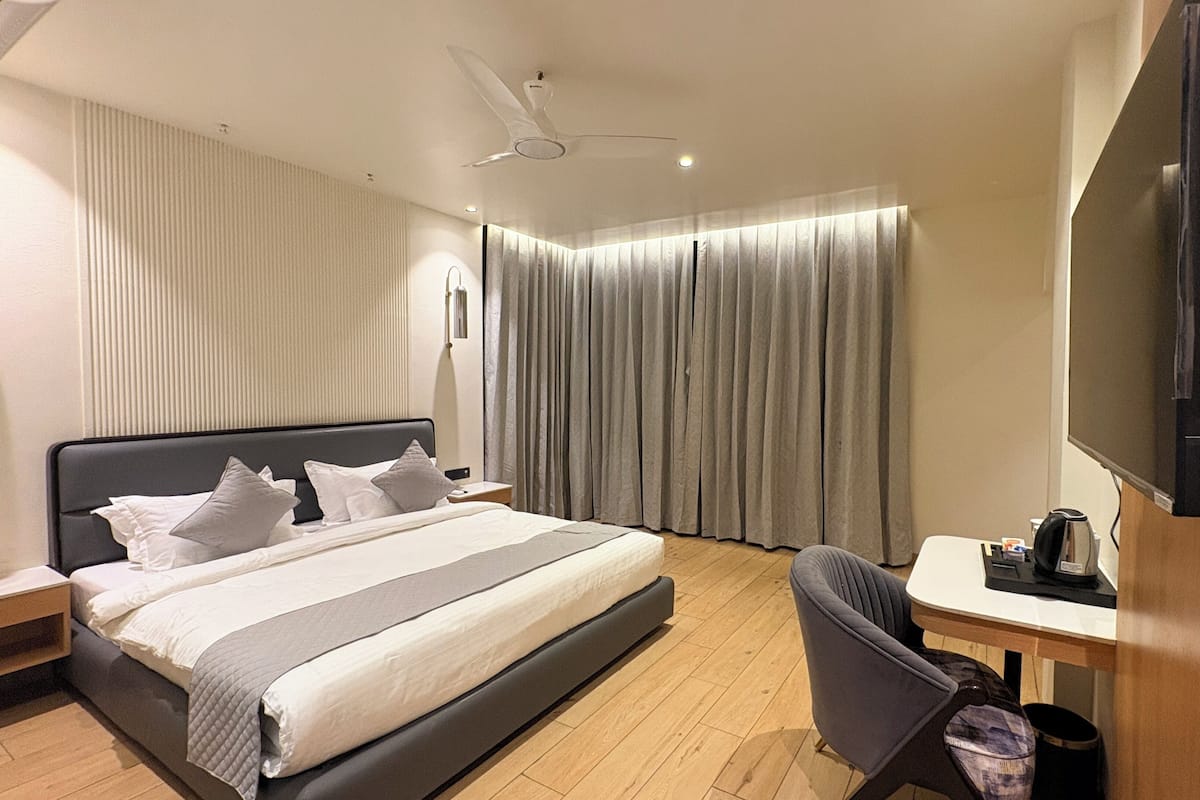 A modern hotel room with a bed, a desk, a chair, a television, and a ceiling fan.