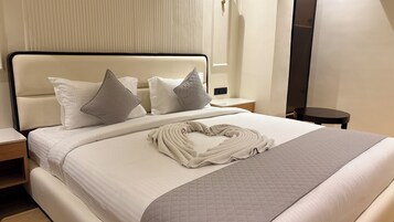 Una cama bien hecha con almohadas, una toalla doblada y una mesita de noche con una lámpara.