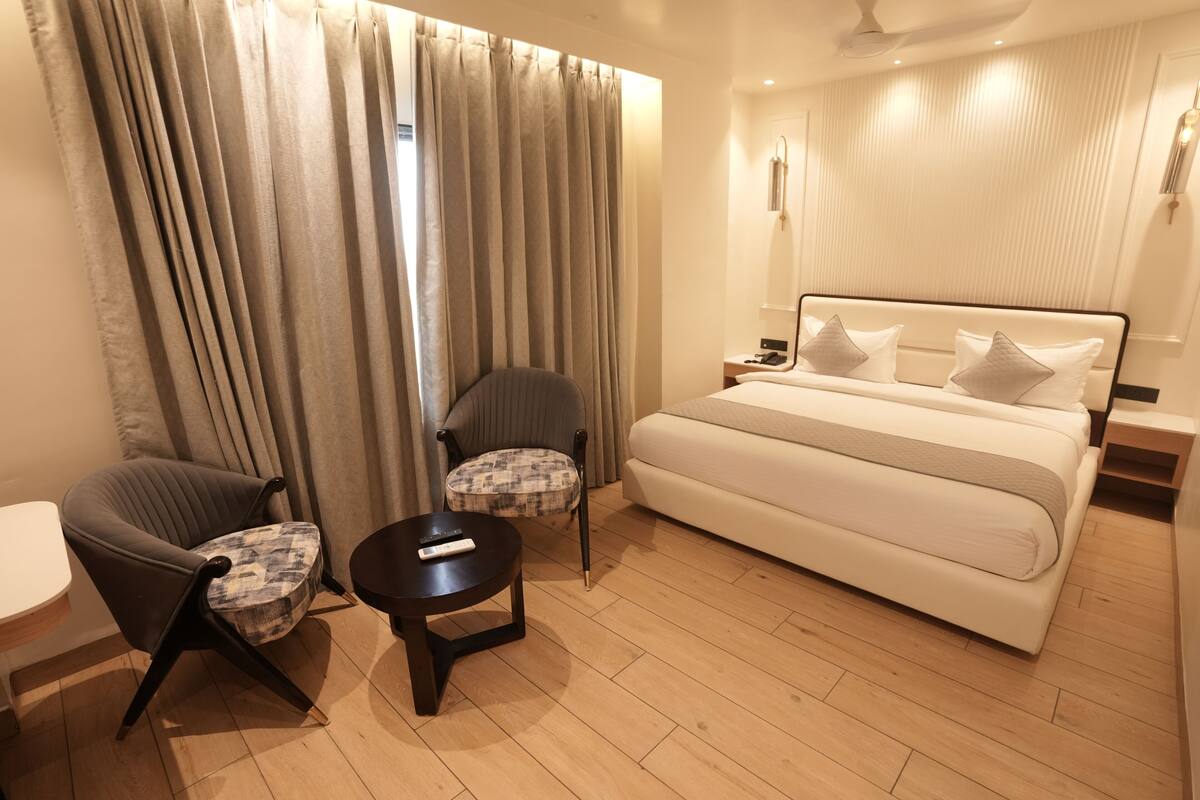 A hotel room with a bed, two chairs, a small table, and a bedside table with a lamp.