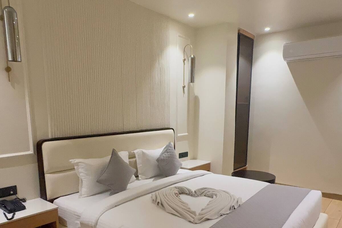 A neatly arranged hotel room with a large bed, a bedside table, a nightstand, a ceiling fan, and a wall-mounted air conditioner.