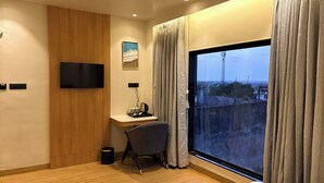 Et hotelværelse med træpaneler, et fladskærms-tv, et skrivebord med stol, et vindue med gardiner og udsigt over bybilledet.