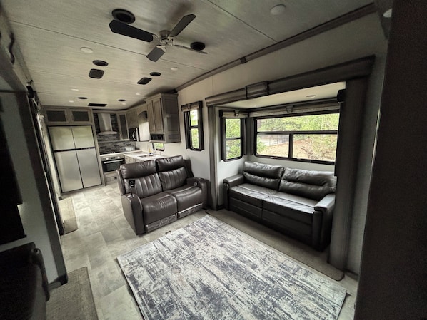 A modern RV interior with a kitchenette, a seating area with a window, and a ceiling fan.
