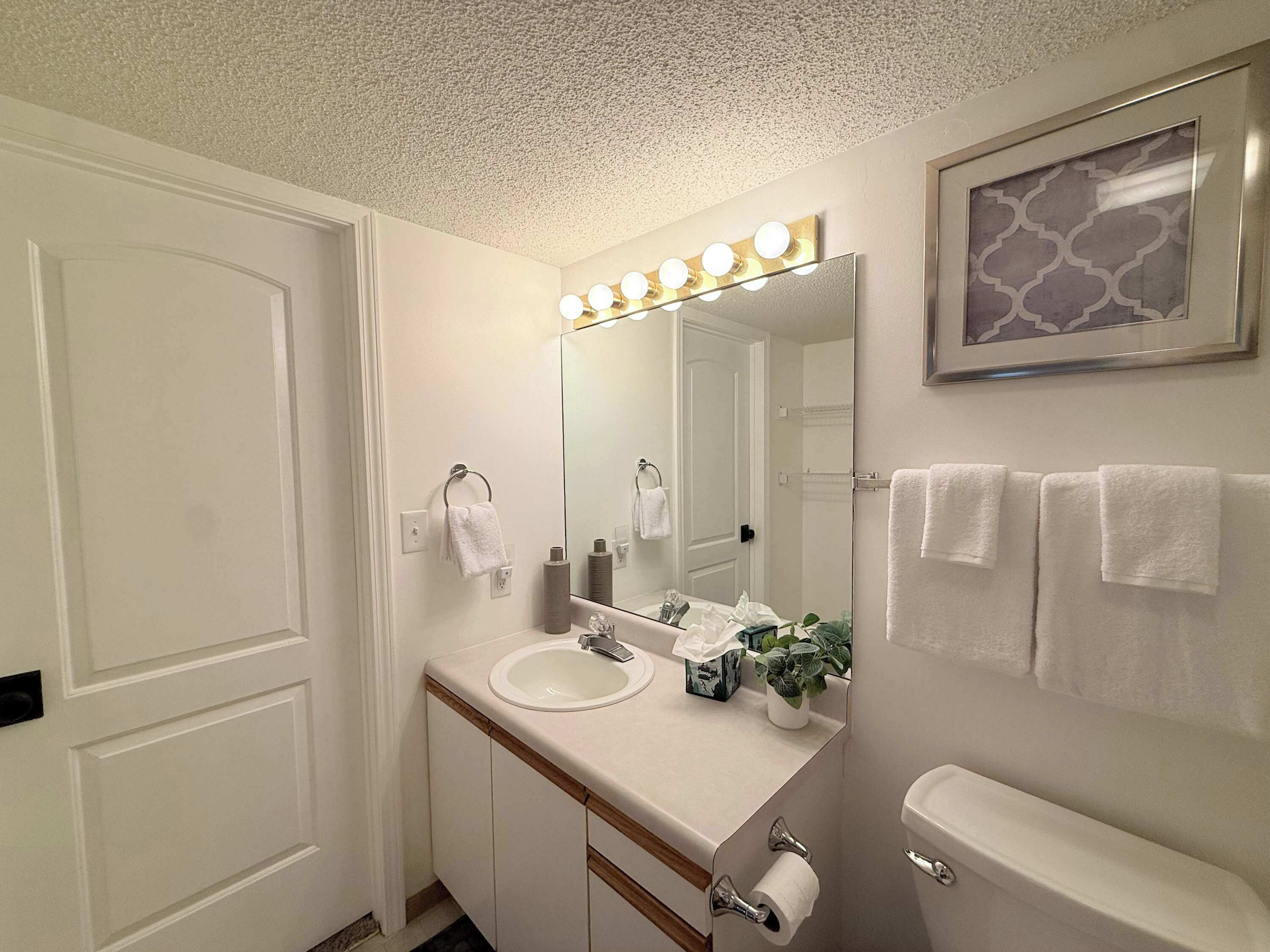 A bathroom with a sink, mirror, vanity, toilet, and towels.
