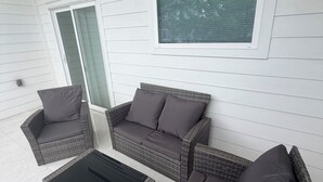 Eine überdachte Terrasse mit Korbmöbeln, darunter eine Couch und Stühle sowie ein Couchtisch.