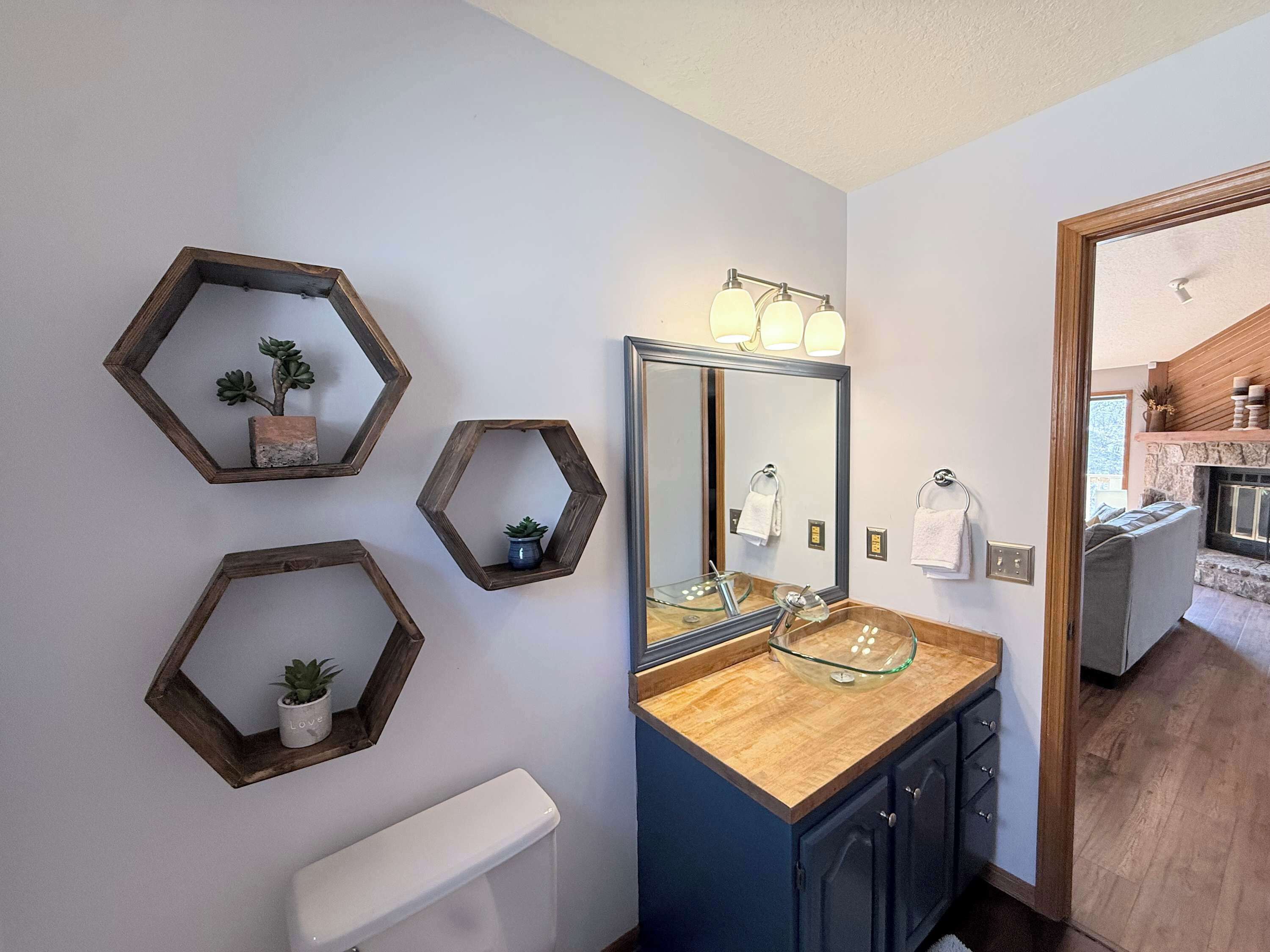 A bathroom with a wooden vanity, a large mirror, and hexagonal shelves with plants.
