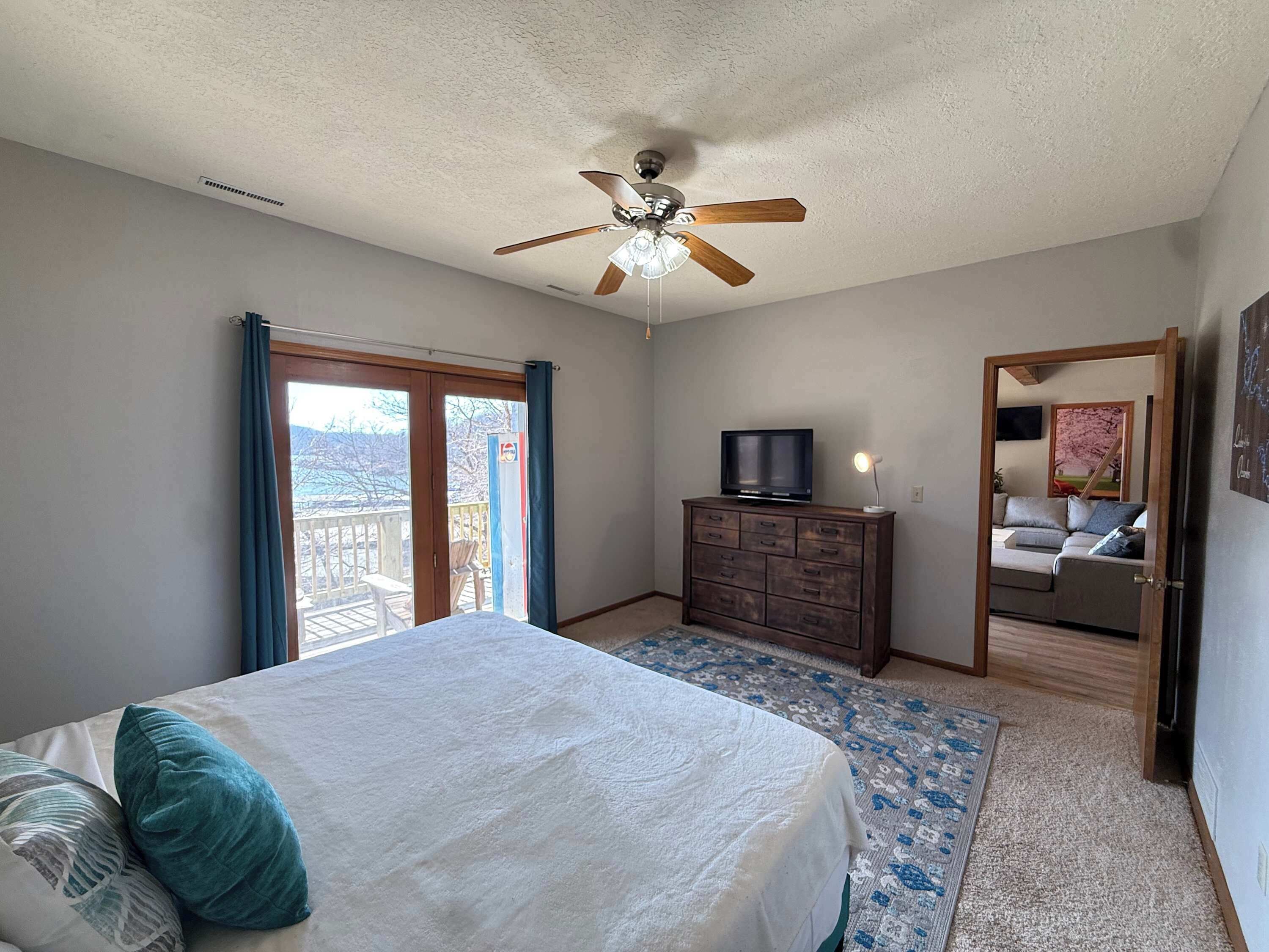A bedroom with a bed, a dresser, a ceiling fan, a television, and a balcony door.