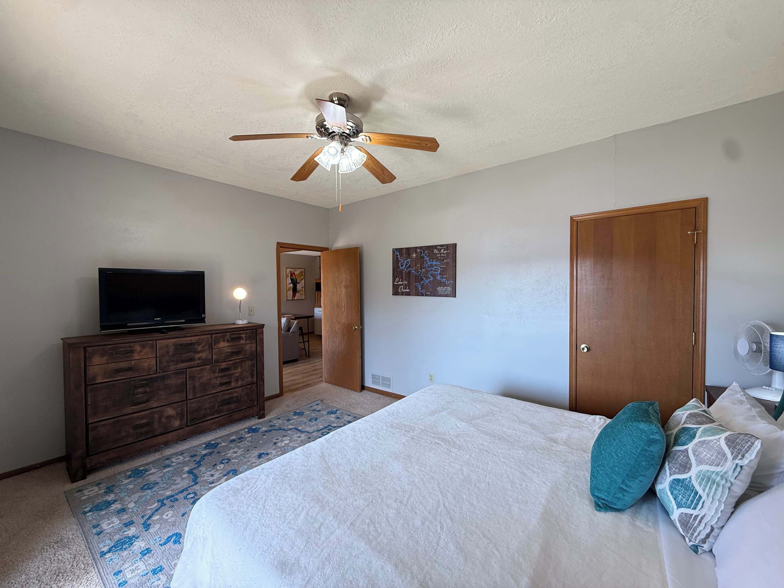 A bedroom with a bed, a ceiling fan, a dresser, a TV, and a door.