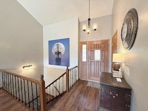 A staircase with a wooden railing, a chandelier, a door with glass panels, and a wall-mounted decorative plate. - Cozy Cove Escape Lakefront (Linn Creek)