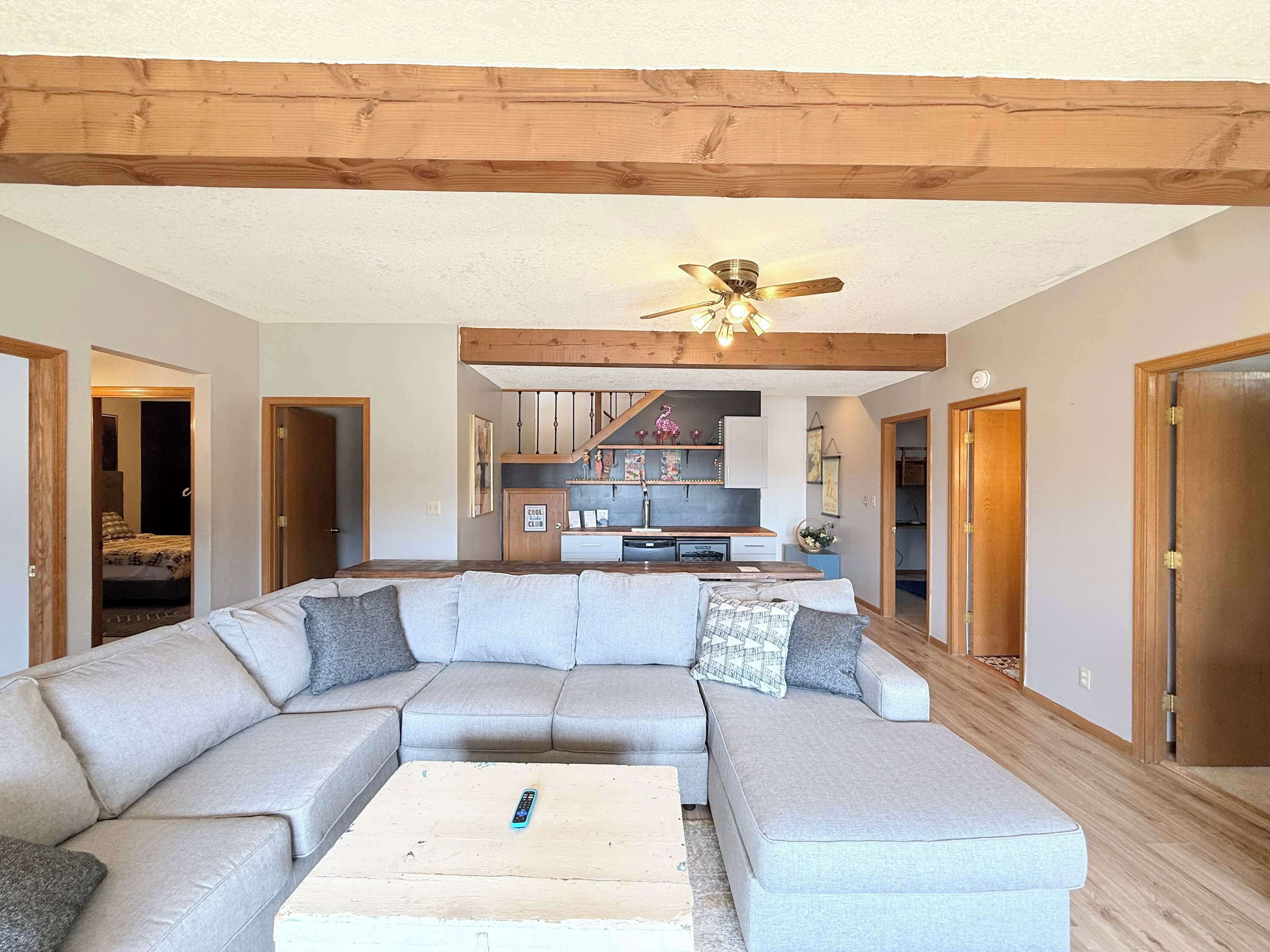 A living room with a sectional sofa, a coffee table, a ceiling fan, and a kitchen area in the background.