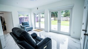 Un salón espacioso con un sofá de cuero negro, un sillón azul y un ventanal corredero que da a un patio trasero.