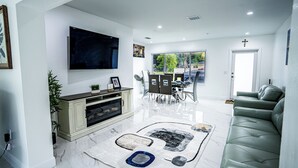 Una sala de estar moderna con una televisión de pantalla plana, un comedor con sillas y una mesa, un sofá y una chimenea.