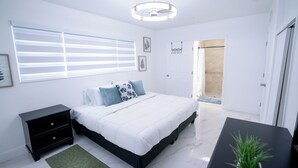 Un dormitorio con cama, mesita de noche y un baño visible a través de una puerta abierta.