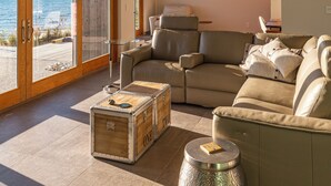 Een ruime woonkamer met een groot raam met uitzicht op zee, een knusse bank en een houten dressoir.