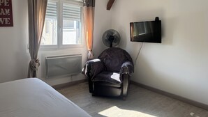 Ein Schlafzimmer mit Bett, Stuhl, Fernseher, einem Fenster mit Vorhängen und einer Heizung.