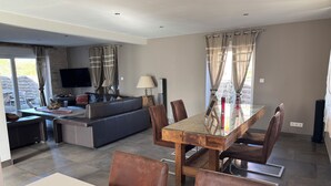 Ein modernes Wohnzimmer mit Sofa, Fernseher und Essbereich mit Stühlen und Tisch.