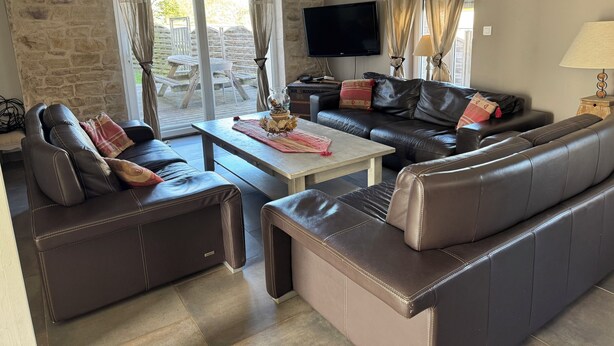Ein Wohnzimmer mit Steinsandsteinwand, Ledersofas, einem Flachbildfernseher und einem Tisch mit einer Vase.