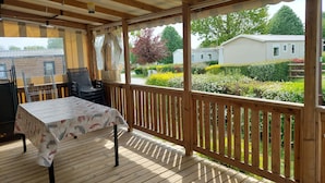 Uma área externa coberta com mesa e cadeiras, um deck de madeira e vista para uma área residencial com casas e vegetação.