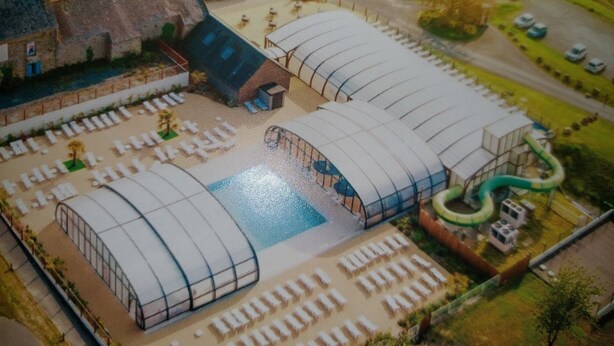 Maquete de um edifício grande com duas estruturas curvas imponentes, um pátio central e uma área verde com um elemento aquático.