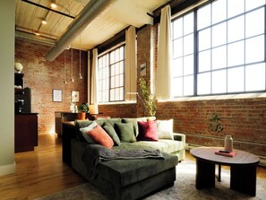 A living room with a sofa, a coffee table, and a brick wall. - 214 Cooperage | Stylish 1BR Warehouse Loft (Peoria)