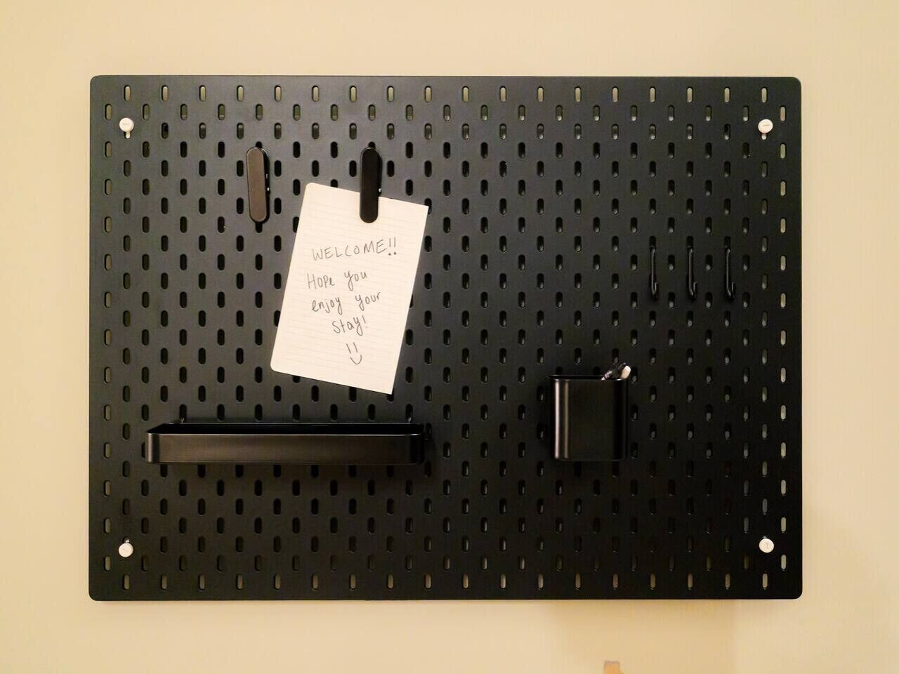 A pegboard with a handwritten note, a black handle, and a black hook.