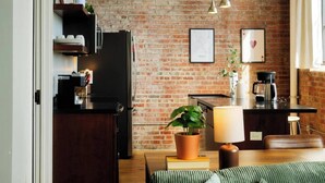 Una cocina con pared de ladrillo, un refrigerador, una cafetera y un comedor con mesa y sillas.
