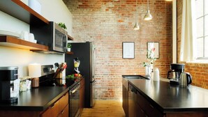 Una cocina con pared de ladrillo, armarios de madera, encimera negra y lámparas colgantes.