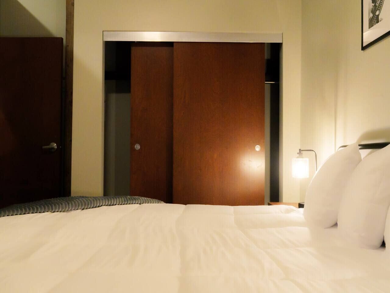 Una habitación de hotel con una cama, un armario de madera y una mesita de noche con lámpara.