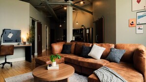 A modern living room with a leather sofa, a round coffee table, and a desk with a chair. - Cooperage 214 | 2BD Boutique Loft Stay (Peoria)