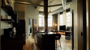 A modern kitchen with a central island, wooden flooring, and a large window providing natural light. - Cooperage 214 | 2BD Boutique Loft Stay (Peoria)
