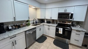 A modern kitchen with white cabinets, stainless steel appliances, and a coffee bar.