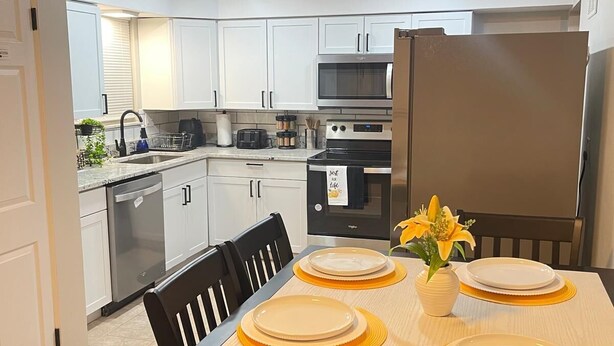 A modern kitchen with white cabinets, a stainless steel refrigerator, and a dining table set with yellow placemats and plates.