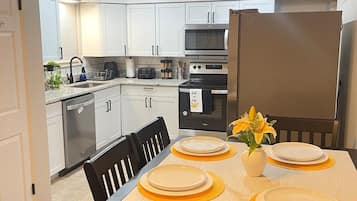 A modern kitchen with white cabinets, a stainless steel refrigerator, and a dining table set with yellow placemats and plates.