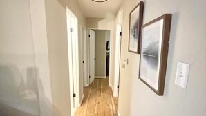 A hallway with wooden flooring, white walls, and framed pictures.