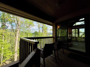 Eine Holzterrasse mit Geländer, einem Stuhl und Blick auf eine bewaldete Gegend.
