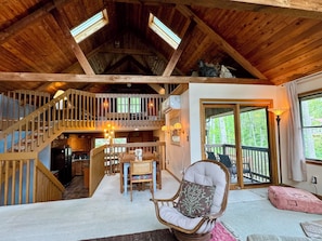 Ein großzügiger Loft-Raum mit hoher Decke, Holzbalken, Essbereich, einer Treppe und einem Balkon mit Blick ins Freie.