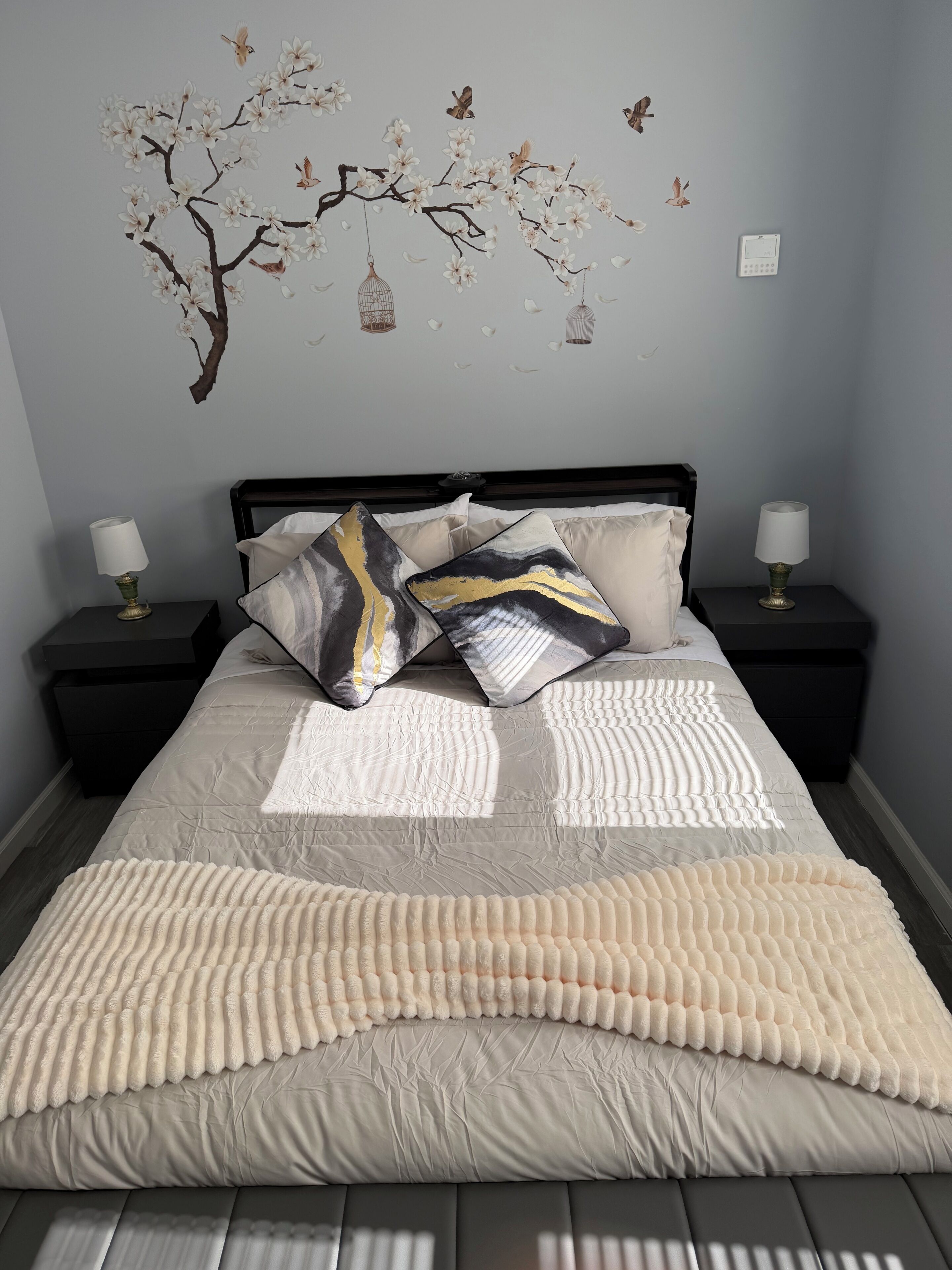 Een slaapkamer met een bed, twee nachtkastjes, een wanddecoratie en een thermostaat.