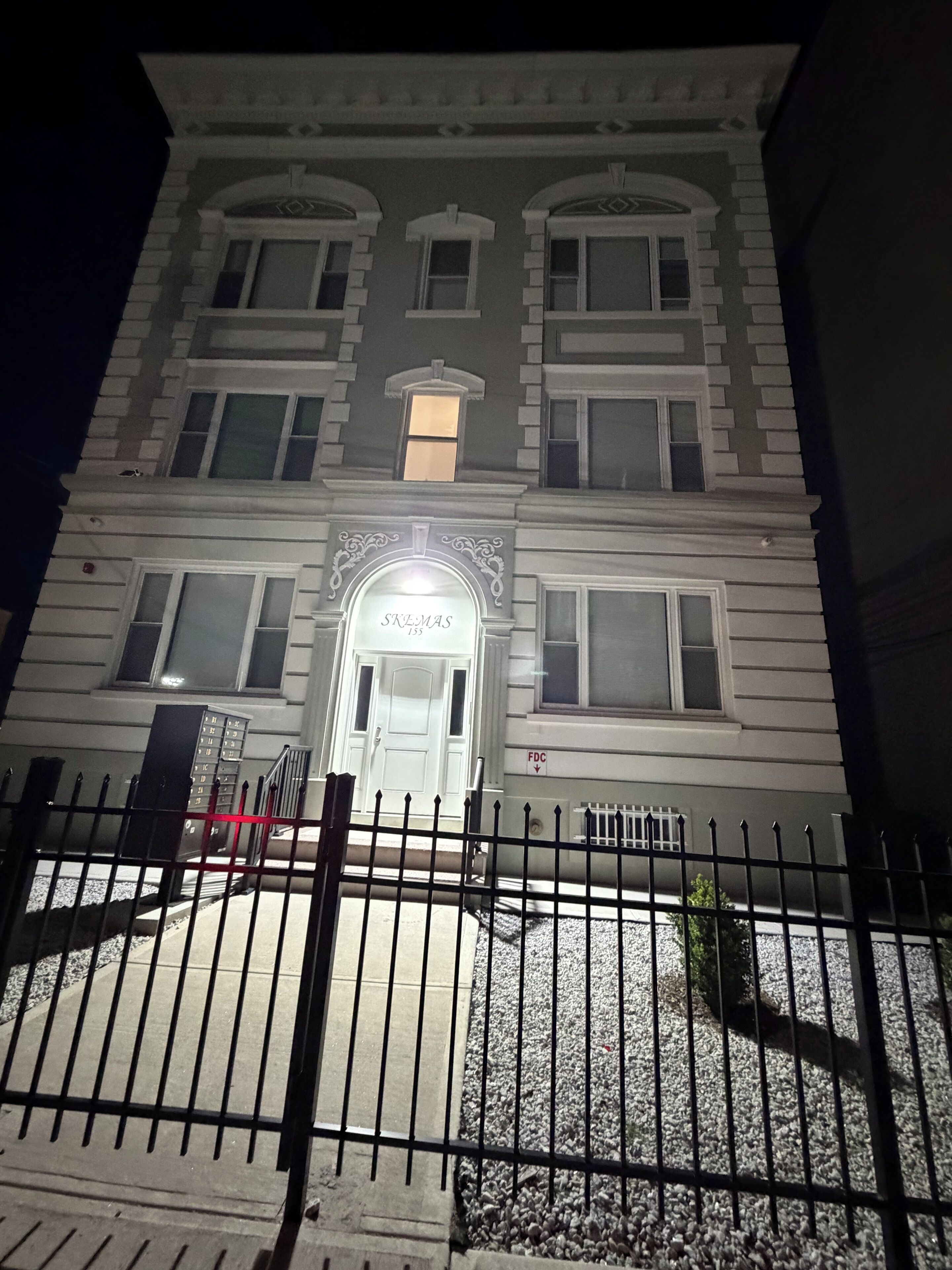 Un edificio de varios pisos con una entrada destacada, un camino de acceso con portones y un letrero sobre la puerta.