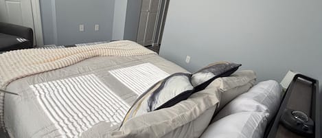 Un dormitorio con cama, mesita de noche, televisor montado en la pared y una puerta.