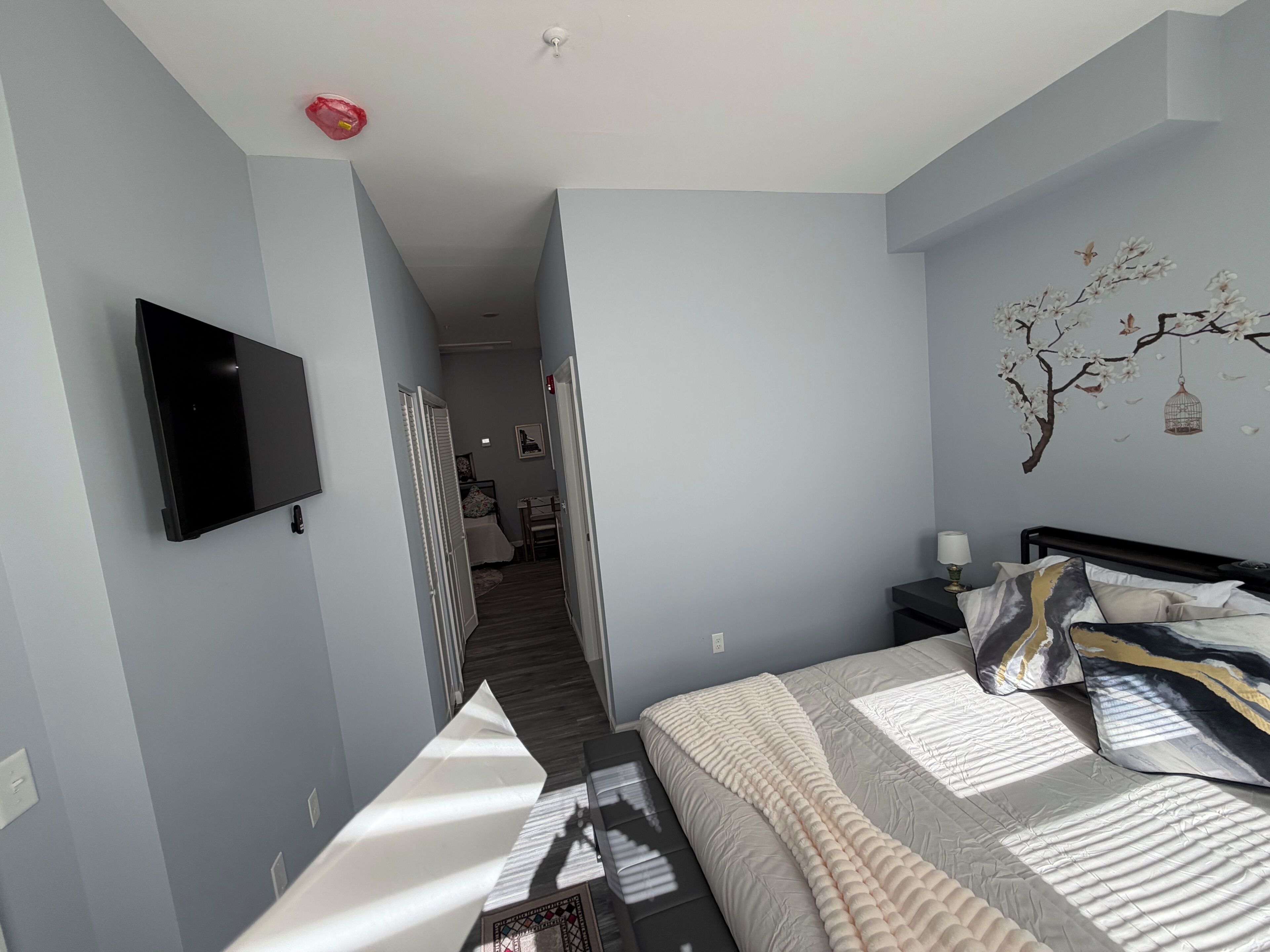 Un dormitorio con cama, televisión montada en la pared, una mesita y una mesita de noche.