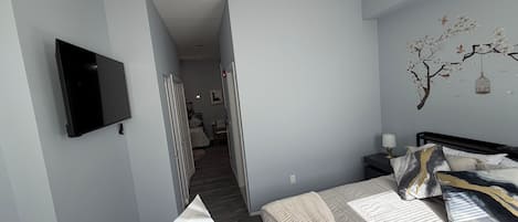 Un dormitorio con cama, televisión montada en la pared, una mesita y una mesita de noche.
