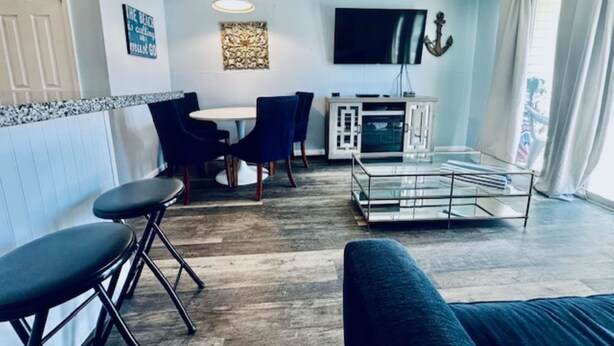 A living room with a sofa, a coffee table, a TV, and a dining area with chairs and a table. - Sandy Seawall Escape Resort (Galveston)