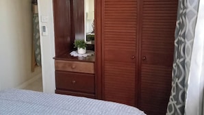 Un dormitorio con una cama, un armario de madera con espejo y una planta pequeña en la cómoda.