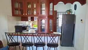 Una cocina con armarios de madera, un refrigerador y una zona de comedor con sillas.