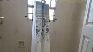 Un baño con inodoro, cortina de ducha estampada y ventana con barrotes.